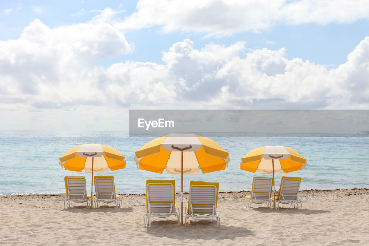 Deck chairs at beach against sky