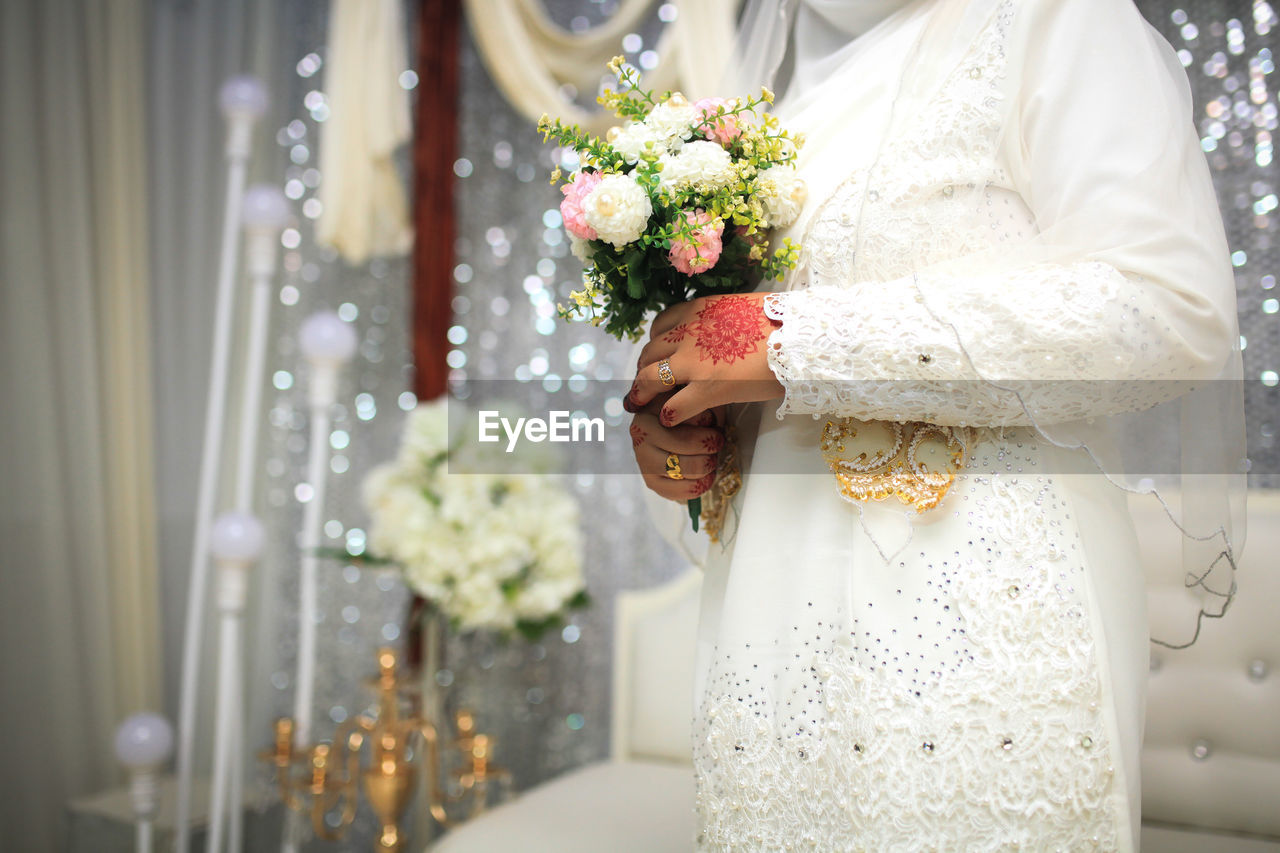 wedding dress, bride, wedding, newlywed, celebration, event, adult, flower, ceremony, life events, women, flower arrangement, flowering plant, bouquet, dress, one person, floristry, wedding ceremony, gown, plant, clothing, bridal clothing, midsection, yellow, white, married, indoors, emotion, standing, love, nature, young adult, positive emotion, female, decoration, happiness, floral design, fashion, holding, lifestyles, rose, tradition, elegance, beauty in nature, veil, traditional clothing, formal wear, beginnings