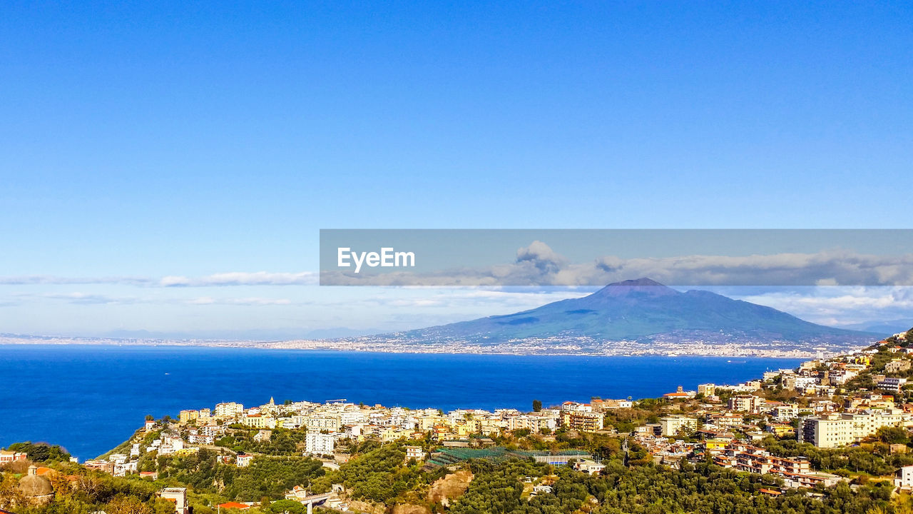 High angle view of city by sea against blue sky