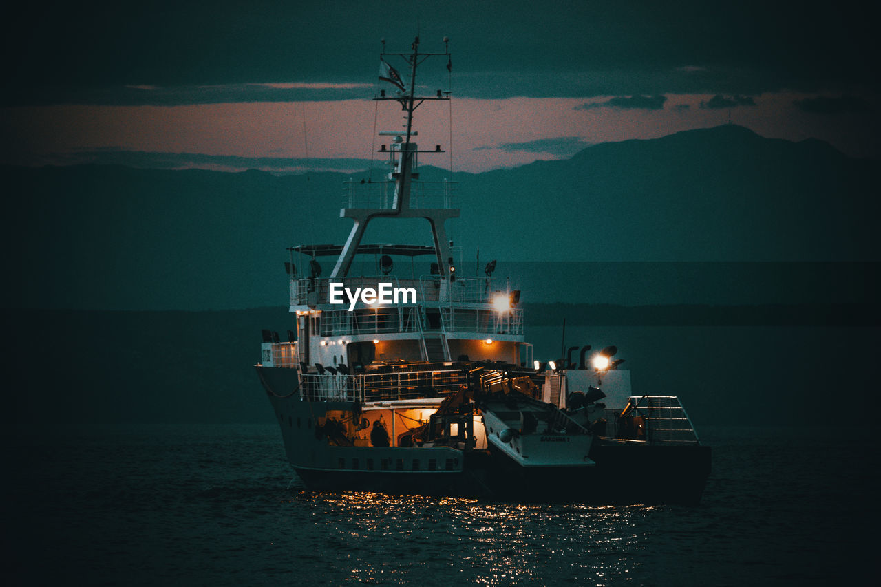 Illuminated ship in sea against sky at dusk