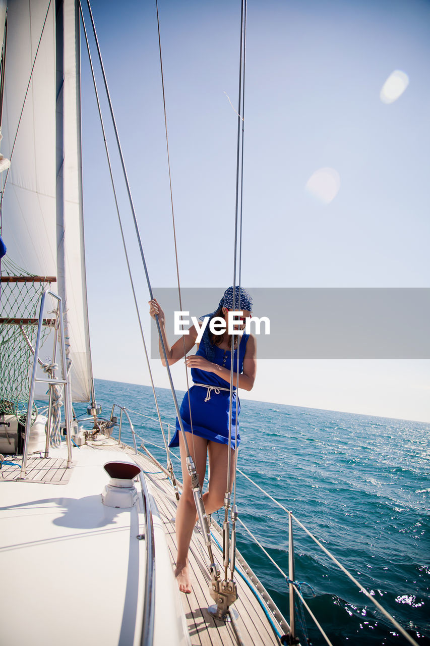 Young woman on nose of the white yacht in a nautical theme. blue jacket, blue scarf and sunglasses.