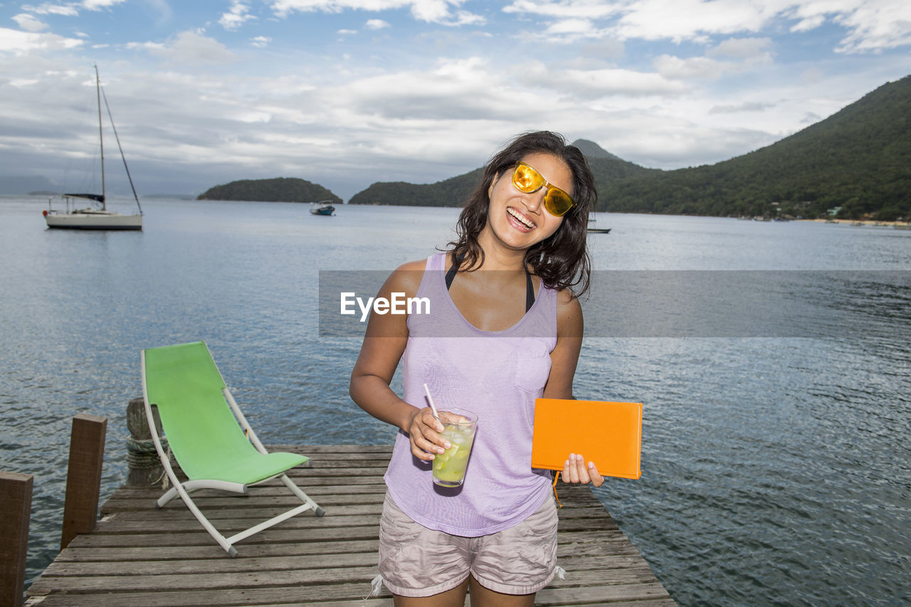 Woman holding drink on pier at the tropical island of ilha grande