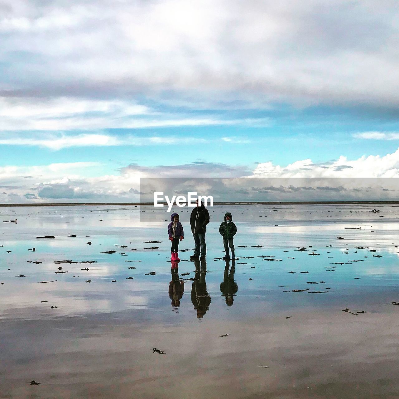 Family standing on wet shore at beach against sky