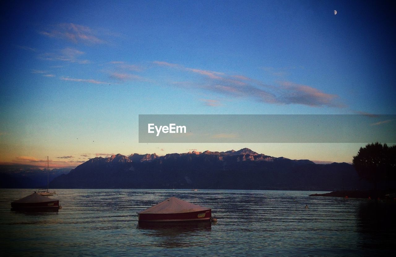 Boats moored in calm lake against mountain range