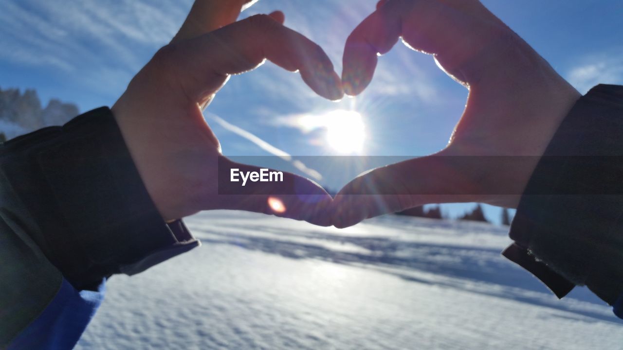 Cropped image of person making heart shape against bright sky