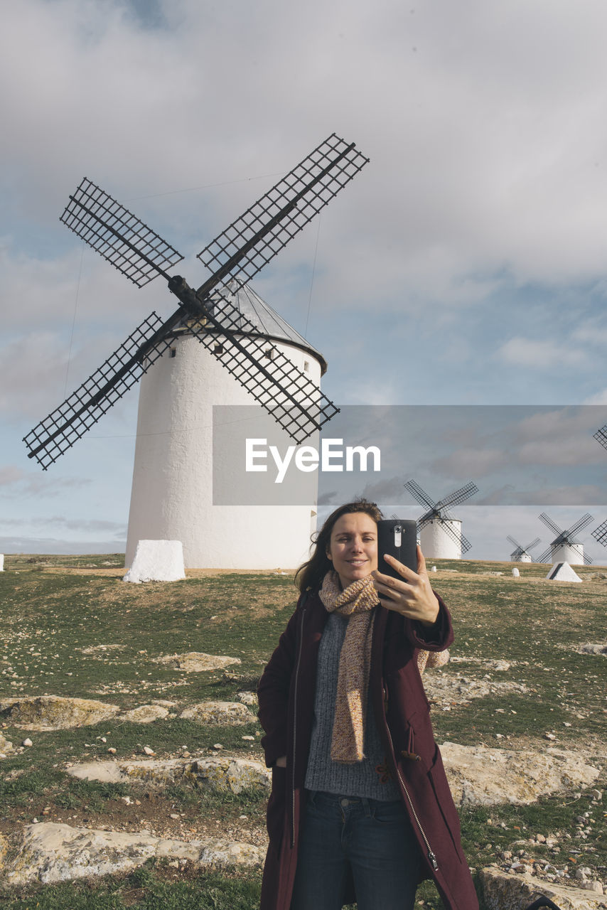 Woman taking selfie while standing against traditional windmills on landscape