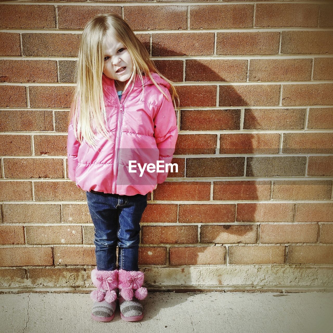 Portrait of small girl making a face while standing against wall