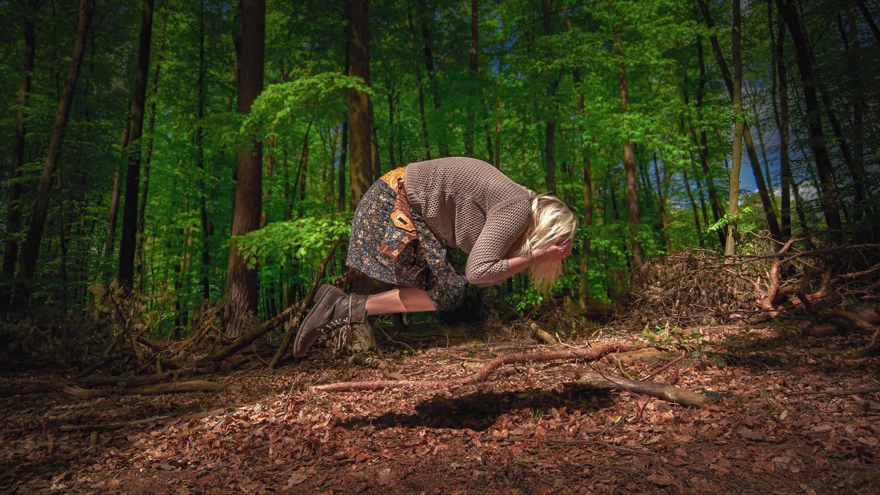 Side view of woman levitating on field in forest