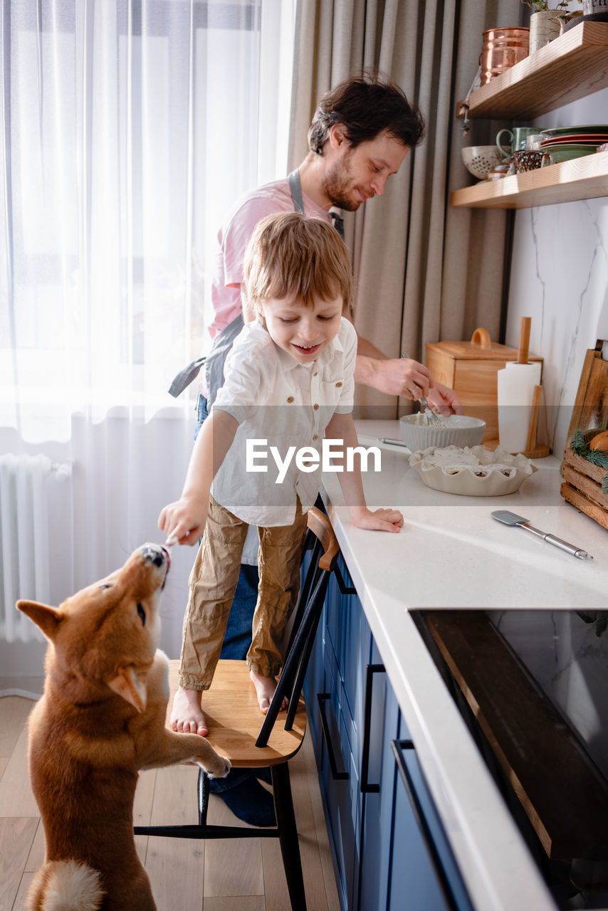 Family fun in the kitchen. cute little boy making whipped cream with his dad and furry friend