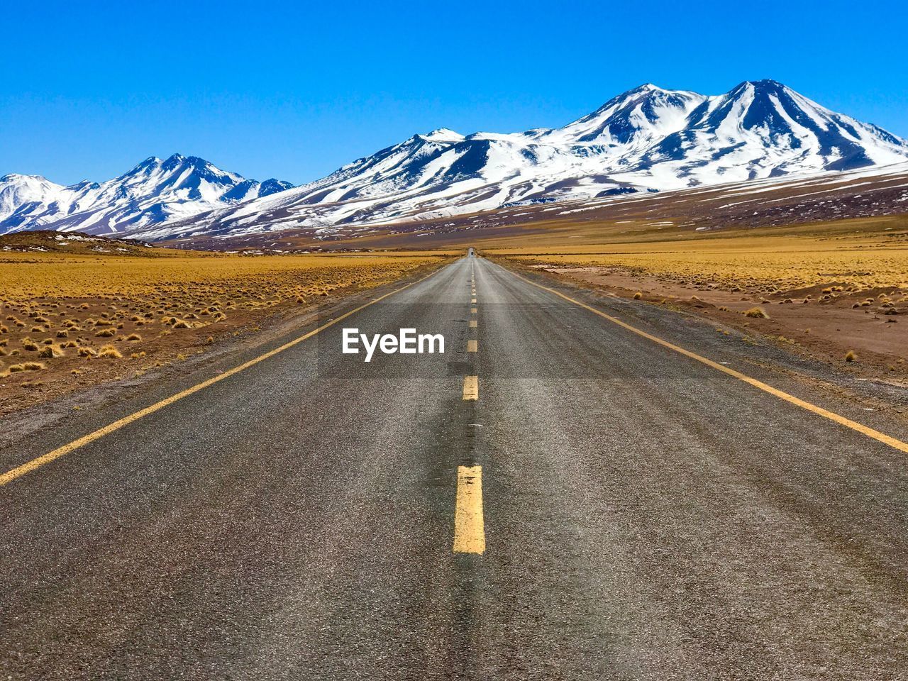 Empty road leading towards snowcapped mountains against clear sky