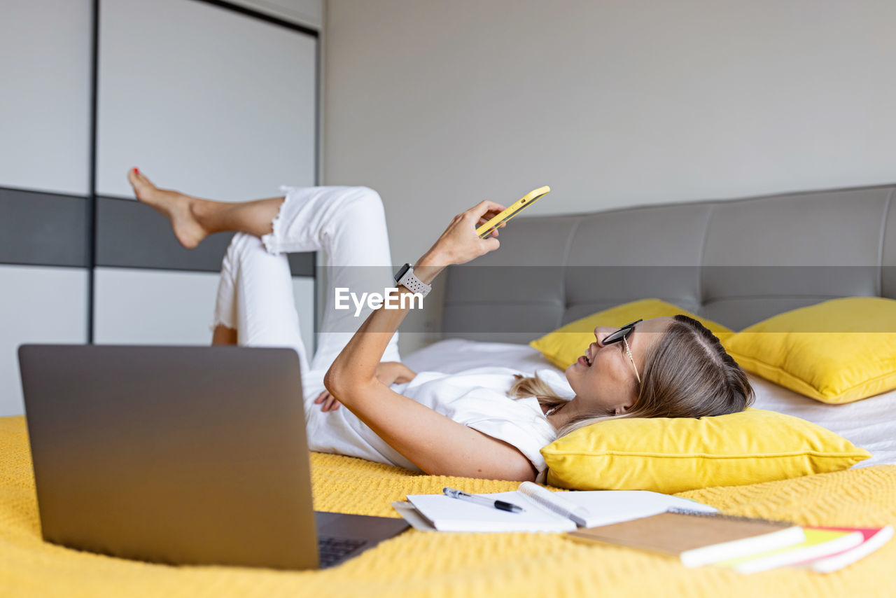 Young woman using laptop while sitting on bed at home