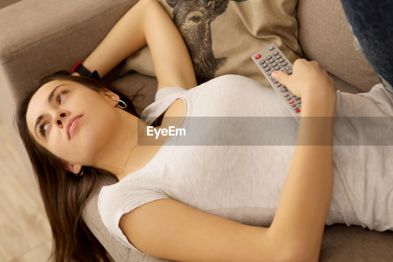 High angle view of woman watching tv while lying on sofa at home