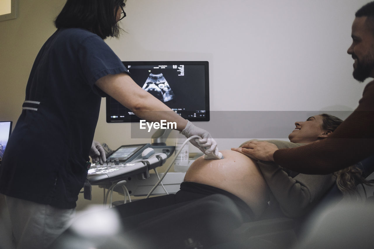 Smiling couple looking at screen while gynecologist doing ultrasound in hospital