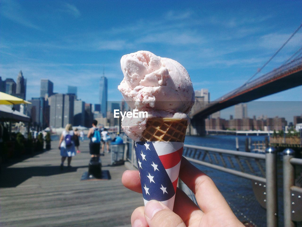 Cropped hand holding ice cream cone on brooklyn bridge against sky