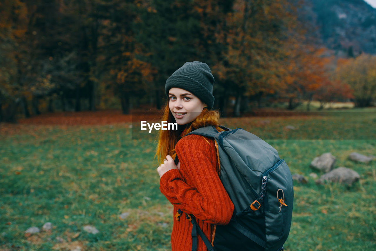 YOUNG WOMAN STANDING BY TREE IN AUTUMN