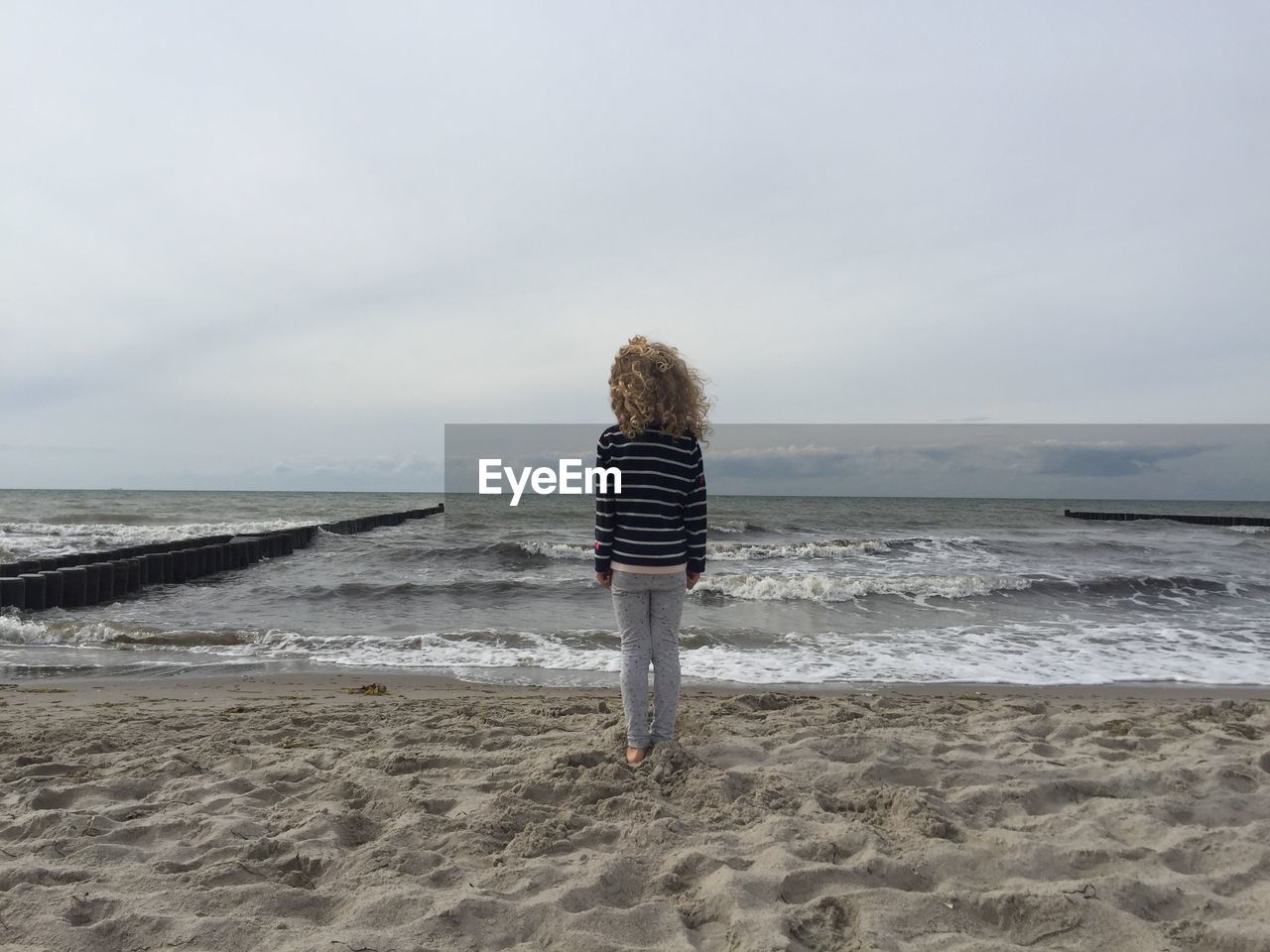 Rear view of woman standing on beach against sky