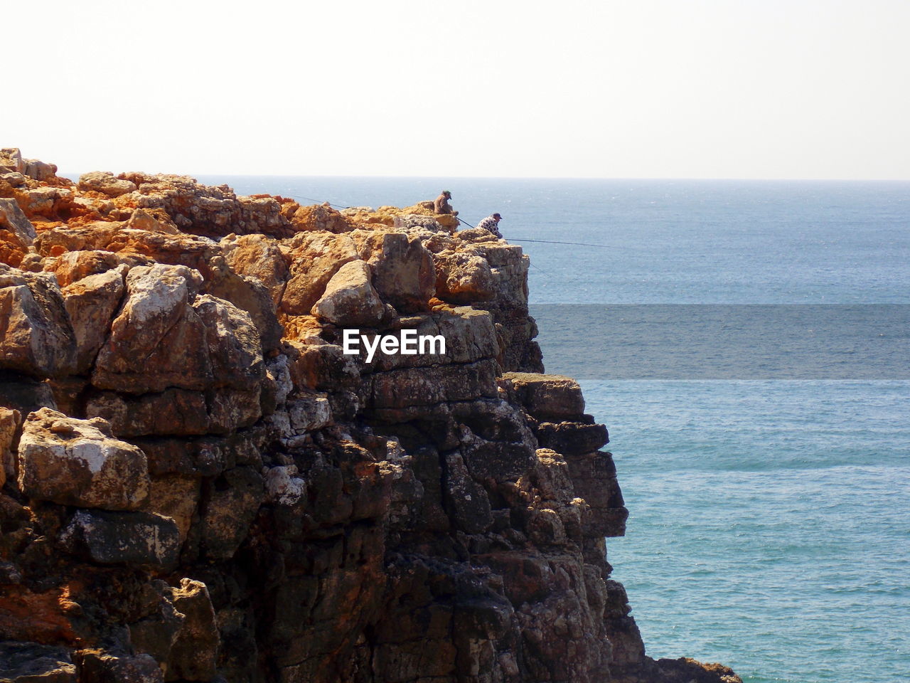 Men on cliff fishing in sea against clear sky