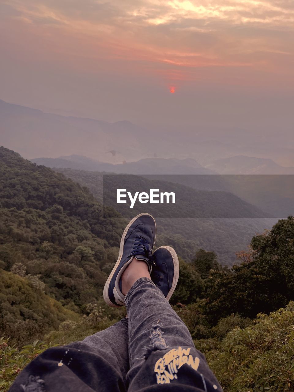 Low section of man on mountain against sky during sunset