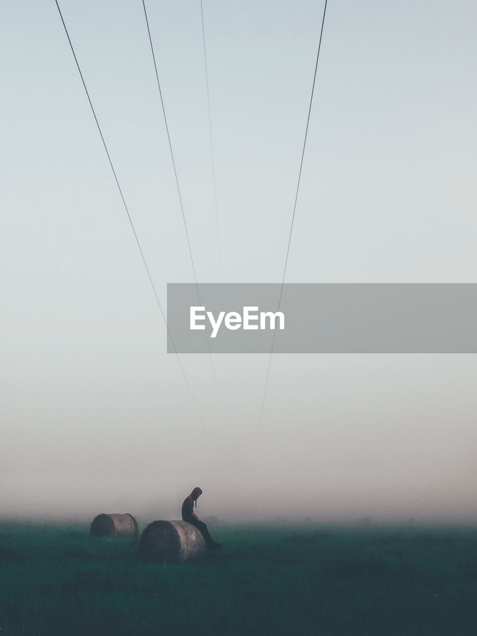 Side view of man sitting on hay bale during foggy weather