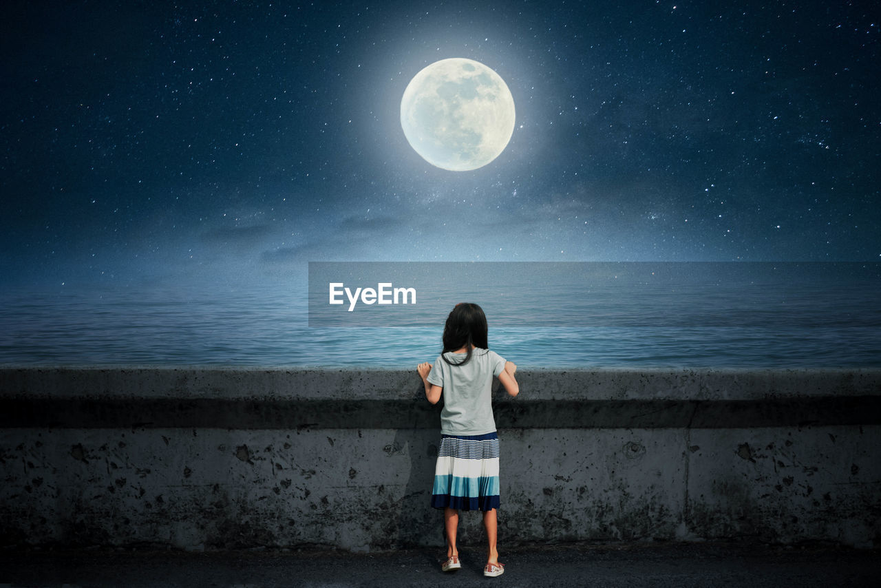 REAR VIEW OF GIRL STANDING AGAINST MOON