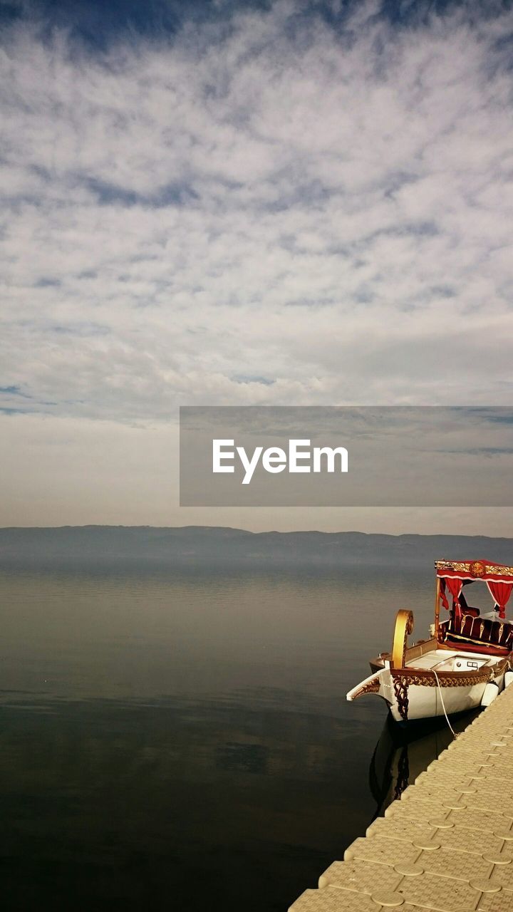 Shikara on lake against cloudy sky