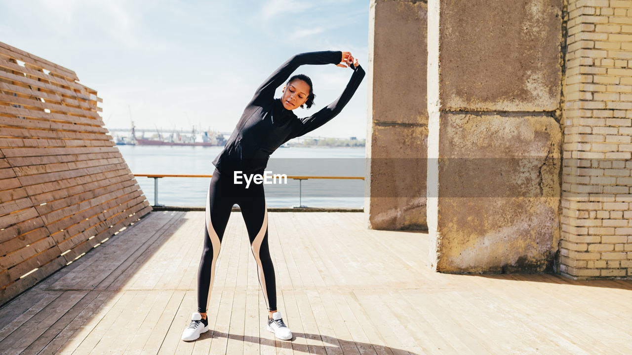 Young woman stretching on footpath against sky