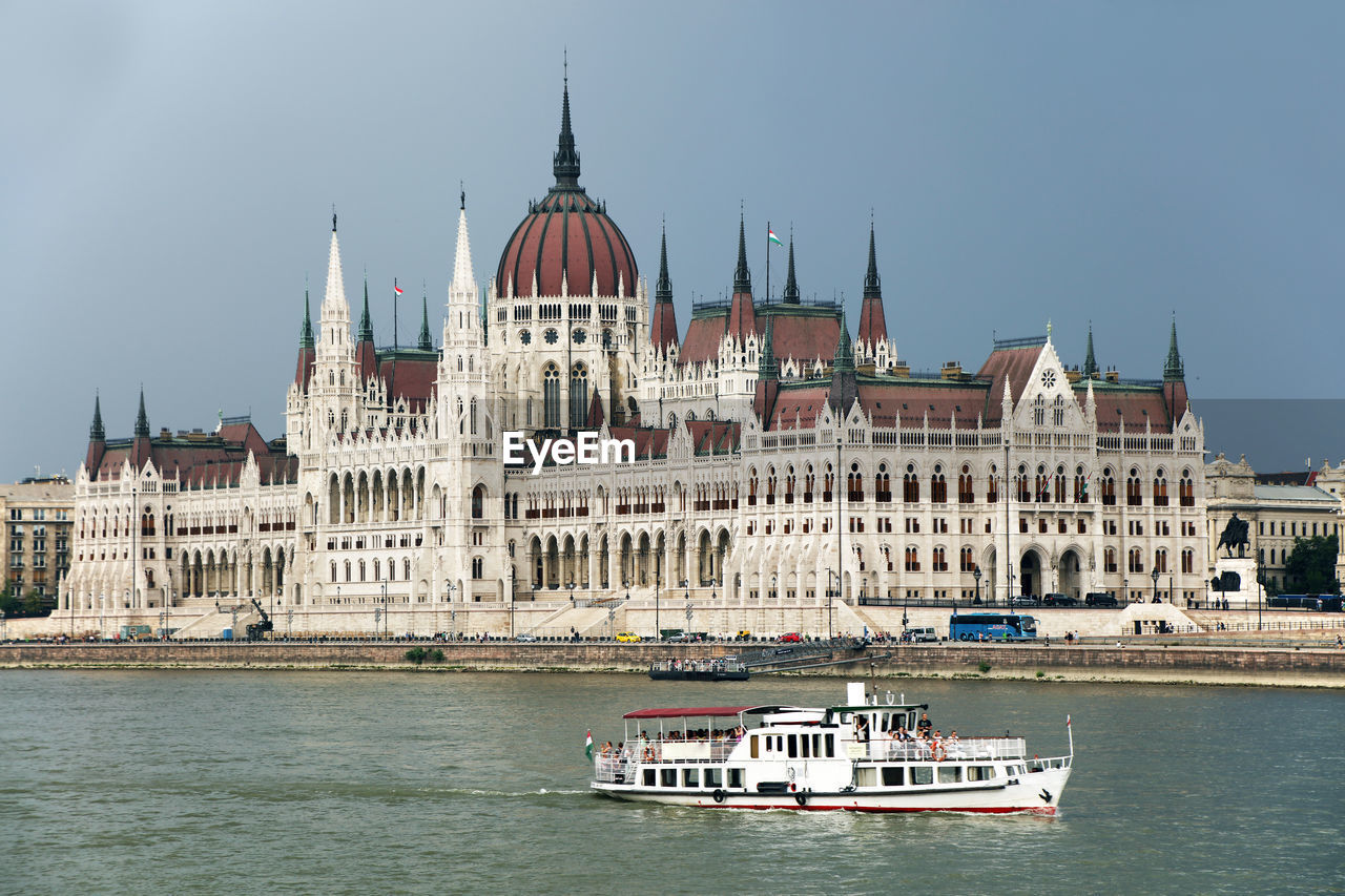 Hungarian parliament building by danube river against sky in city