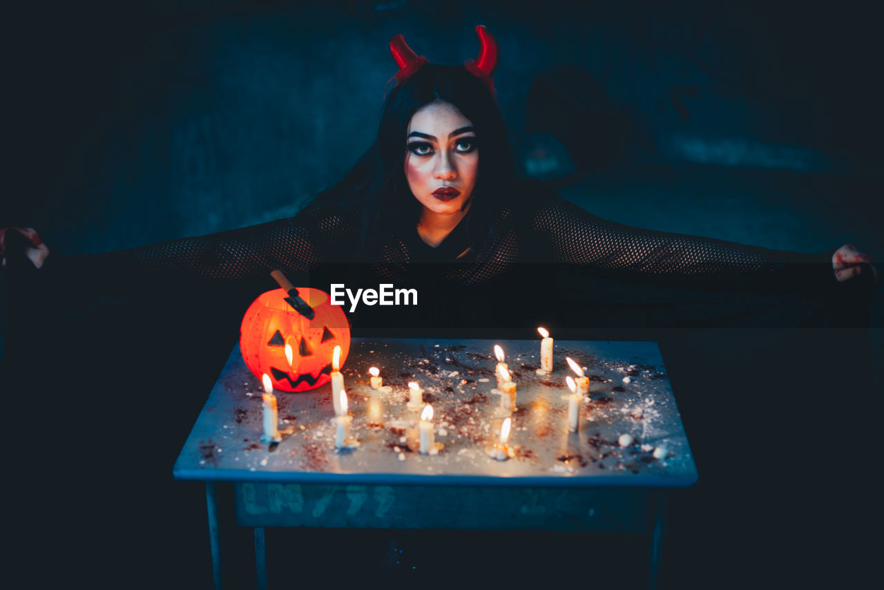 High angle portrait of young woman in witch costume with lit candles on table