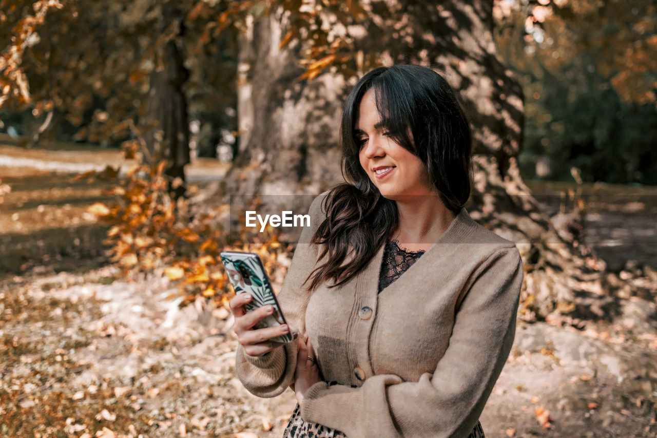 Young woman using mobile phone, autumn, fall, happy, smiling.