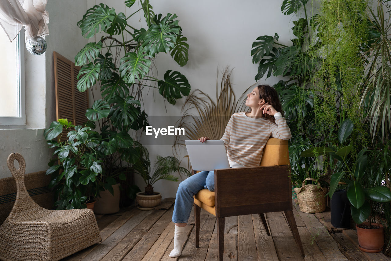 Dreamy woman rest after finished work on laptop look in window sitting in chair at cozy home garden