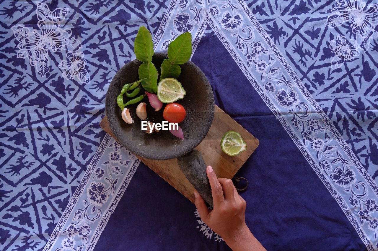 Cropped image of person holding pestle with herbs and spices in mortar on table