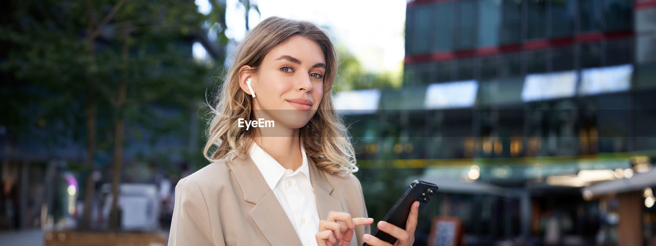 portrait of young woman using mobile phone while standing outdoors