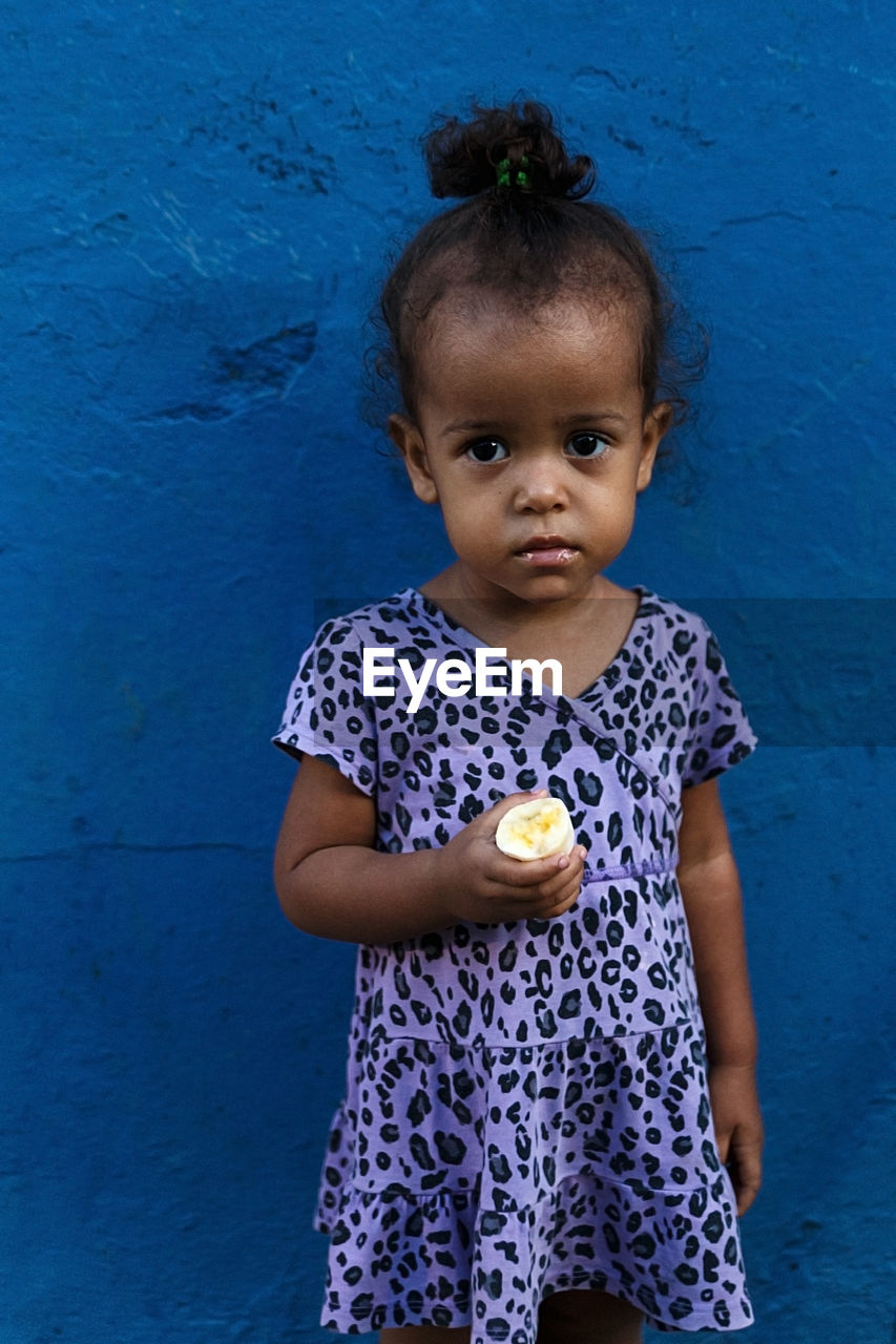 Portrait of girl holding food against blue wall