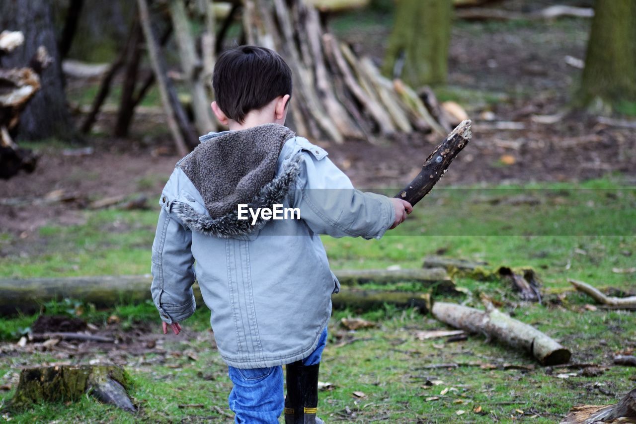 Rear view of boy with wood on field