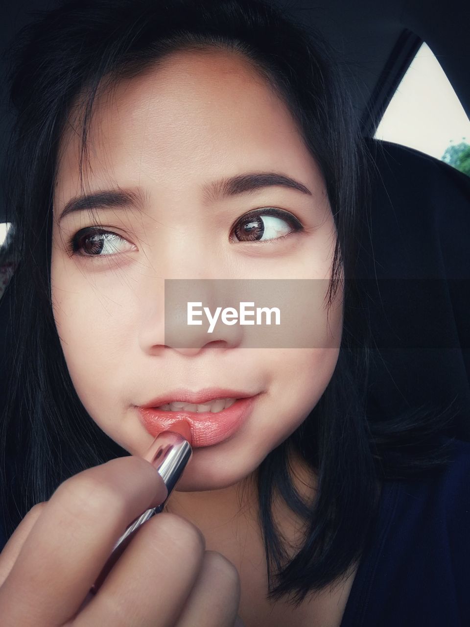 Close-up of young woman applying lipstick in car