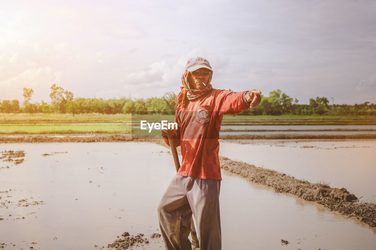 Farmer pointing while standing on field against sky