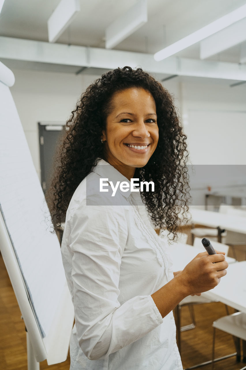 Side view portrait of smiling teacher with curly black hair standing by flipchart in classroom