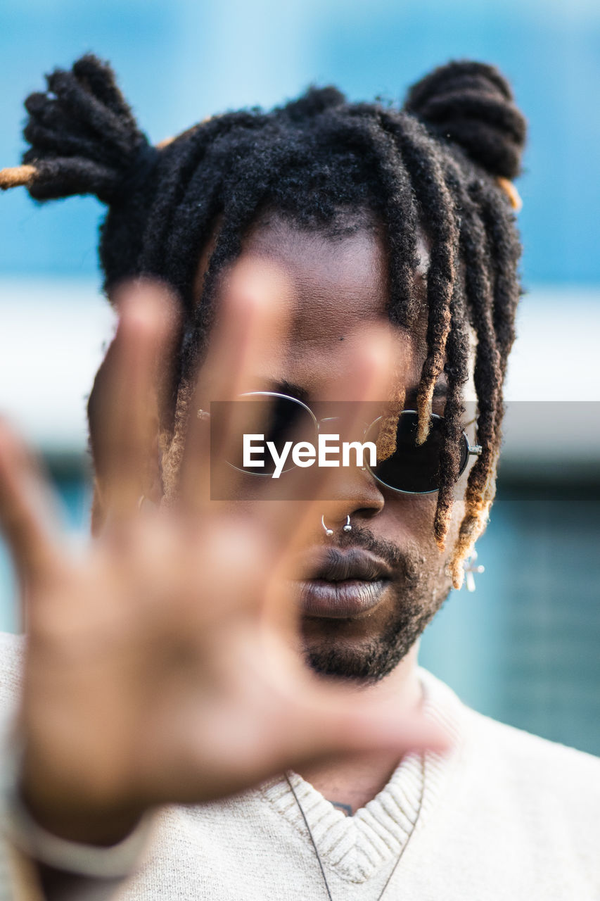 Modern african american guy with dreadlocks in buns and nose piercing outstretching hand toward camera in stop gesture