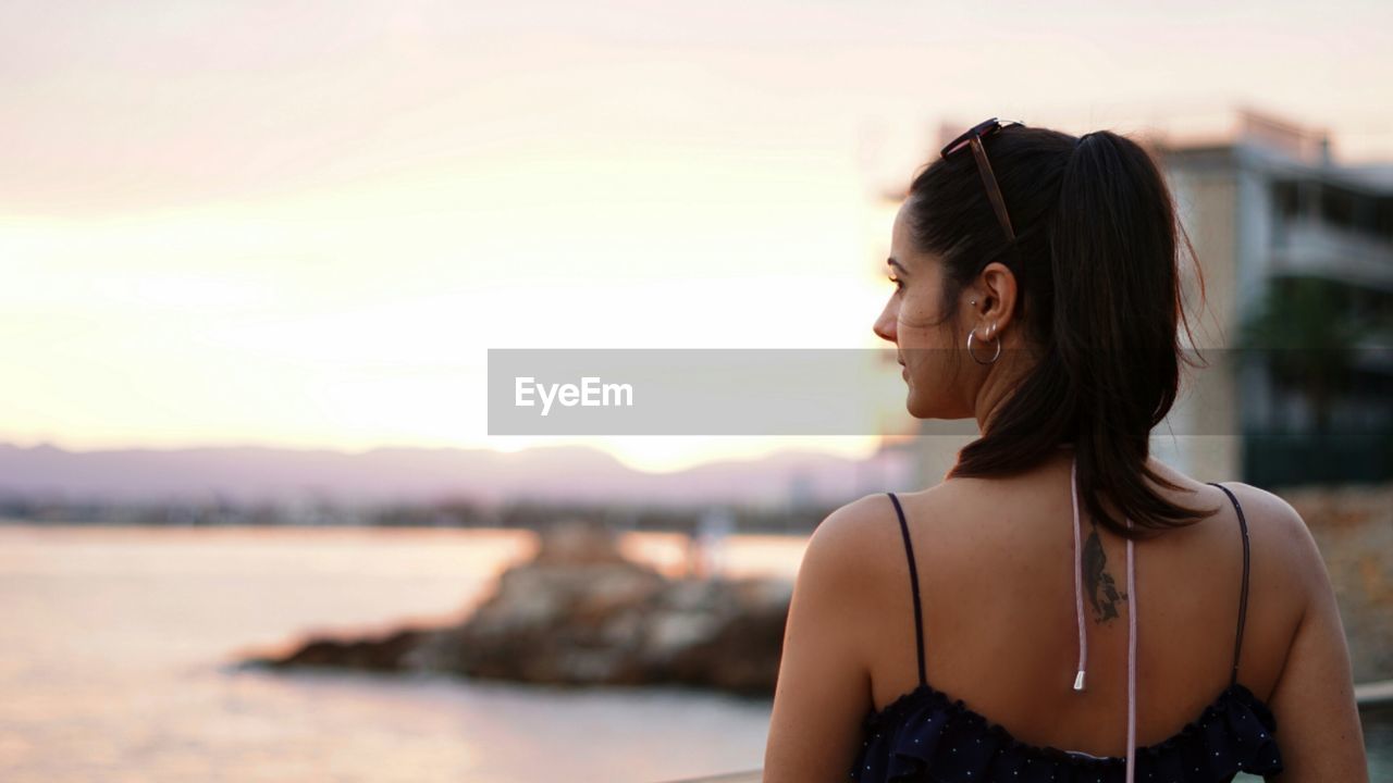 Portrait of smiling young woman looking away againts sea at sunset