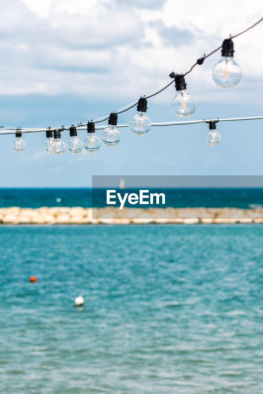 Vintage hanging light bulbs with blue sky, white clouds, blue sea, sail boat and breakwater