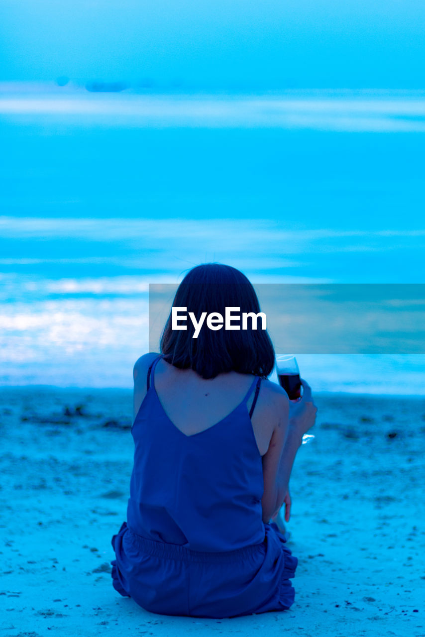 Rear view of woman having drink while sitting at beach