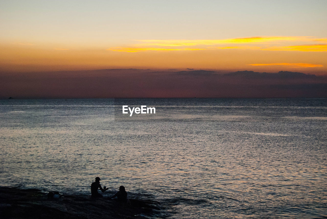 Silhouette people in sea against sky during sunset