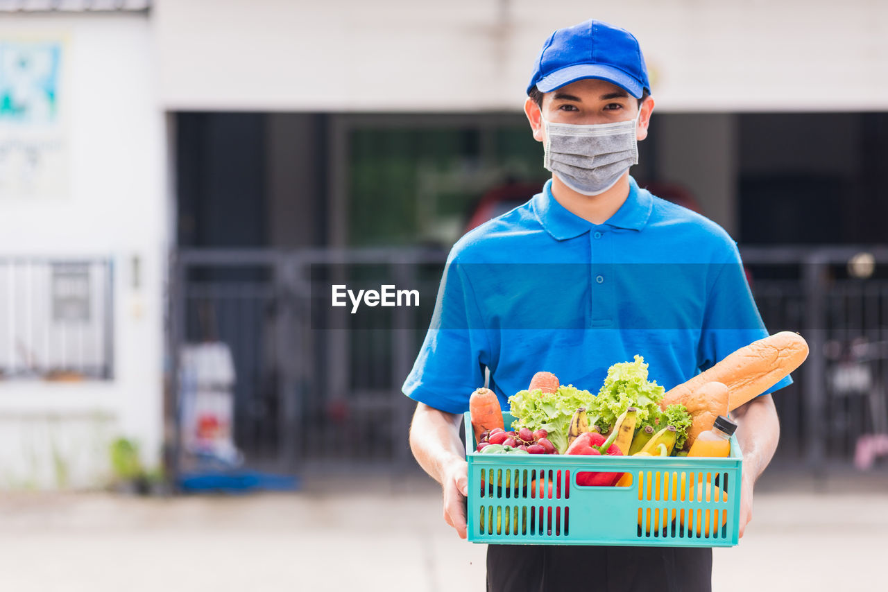Grocery delivery man wearing blue uniform and face mask protect he delivering fresh food vegetable