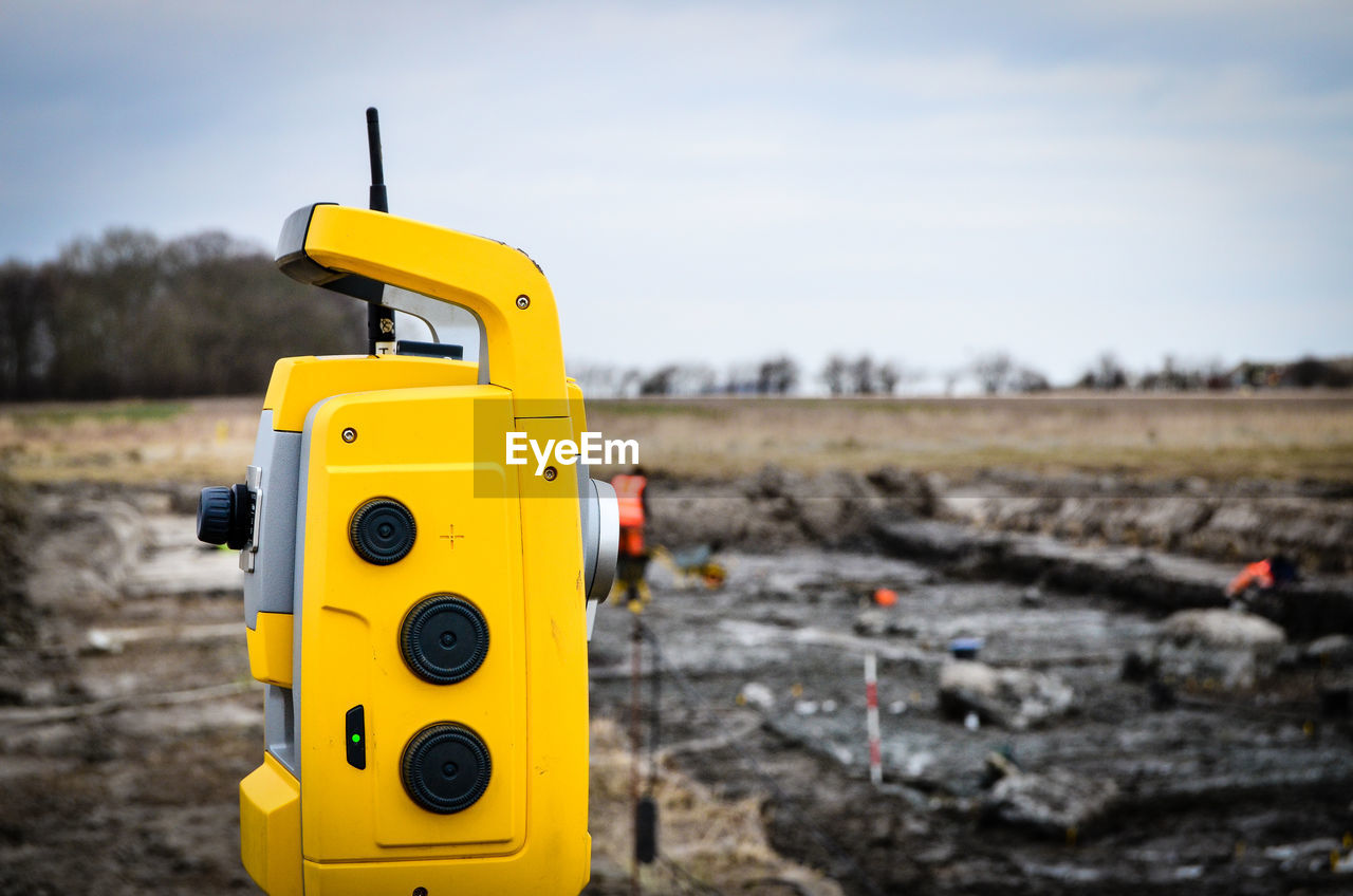 Surveying level on field against sky