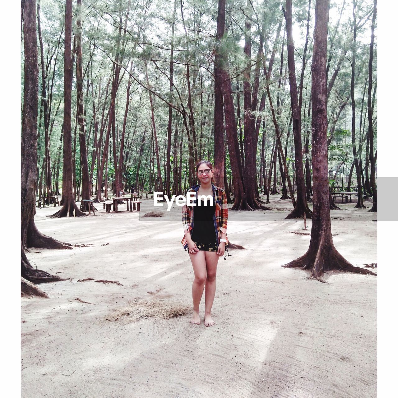 PORTRAIT OF YOUNG WOMAN STANDING ON TREE TRUNK