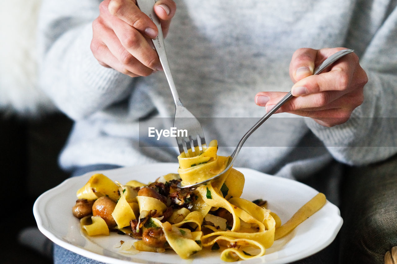 Midsection of person picking pasta with fork