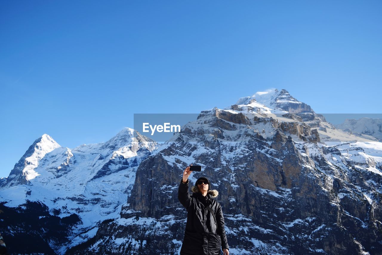 Man taking a selfie on snowcapped mountain against clear blue sky