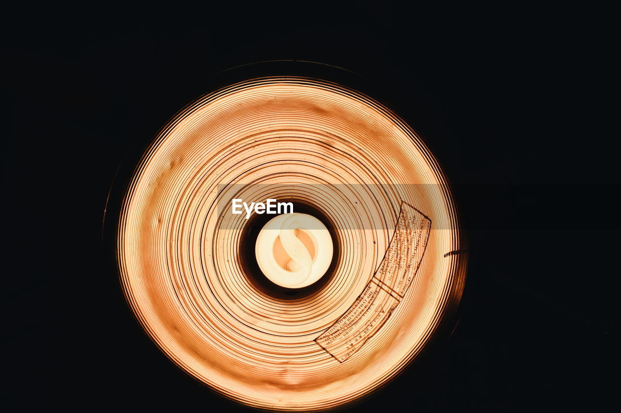 Directly below view of illuminated light bulb against black background