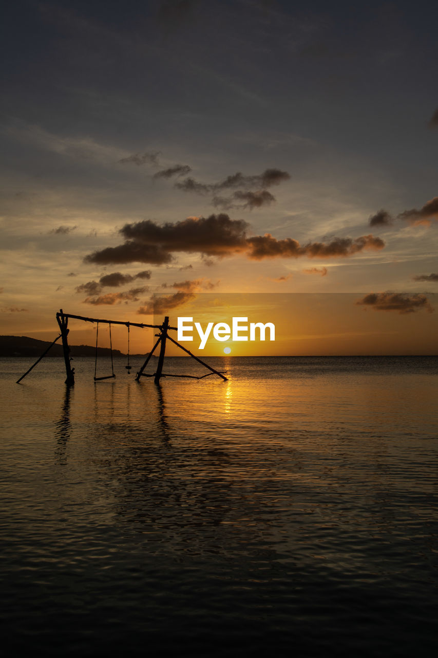 SILHOUETTE WOODEN POSTS IN SEA AGAINST SKY AT SUNSET