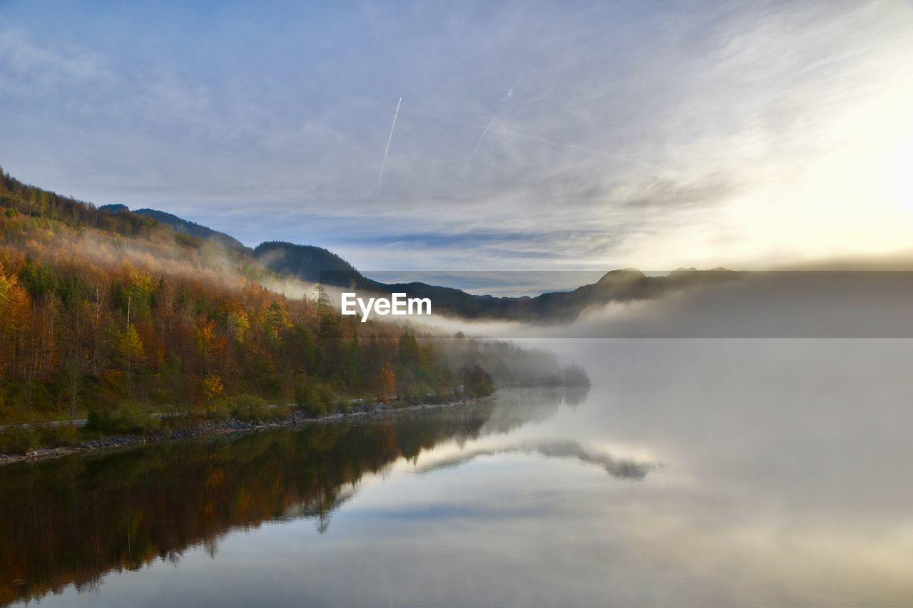Scenic view of lake in forest with fog against mountains and sky
